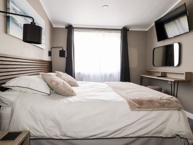 A bedroom with a bed white bedding wall lamps a desk mirror and a wall mounted TV at 63 The Maples Hewas Water near Sticker