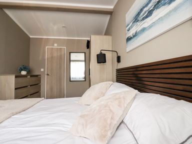 A bedroom with a bed a wooden headboard pillows a dresser a wall mirror and a door at 63 The Maples in Hewas Water near Sticker