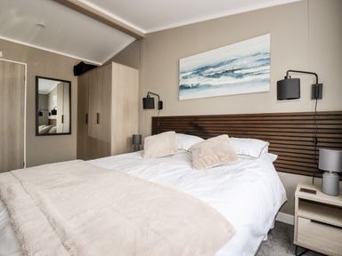 A bedroom with a double bed two beige pillows a beige blanket a wardrobe a mirror two lamps and ocean artwork at 63 The Maples Hewas Water near Sticker