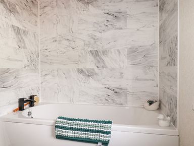 A white bathtub with a green and white towel and wall tiles with a marble pattern at 63 The Maples in Hewas Water near Sticker