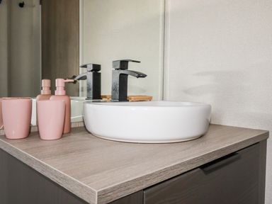 A bathroom countertop with a round white sink black faucet and pink soap dispenser and cup at 63 The Maples in Hewas Water near Sticker
