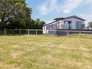 A mobile home with a deck and outdoor furniture on a grassy plot with trees in the background at 63 The Maples in Hewas Water near Sticker