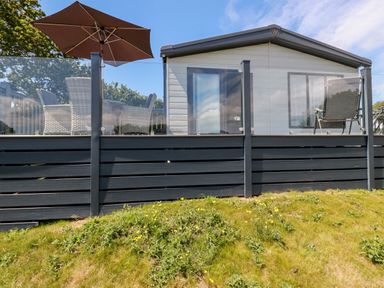 A raised outdoor deck with chairs and an umbrella attached to a mobile home at 63 The Maples Hewas Water near Sticker