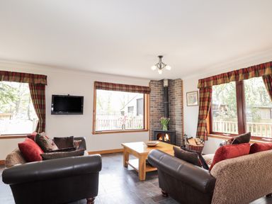 A living room with two sofas a wood burning stove a coffee table and three windows at Lovat Highland Bothy in Beauly