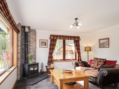 A living room with a wood burning stove next to a window with plaid curtains and a sofa with cushions at Lovat Highland Bothy in Beauly