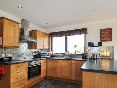 A kitchen with wooden cabinets, black countertops, a window above the sink, and various appliances at Lovat Highland Bothy in Beauly