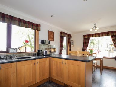 A kitchen and dining area with wooden cabinets and a dining table with chairs at Lovat Highland Bothy in Beauly