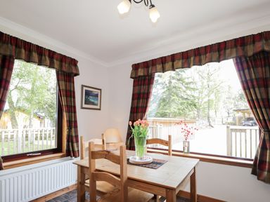 A dining area with a wooden table and chairs near windows with plaid curtains at Lovat Highland Bothy in Beauly
