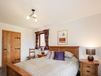 A bedroom with a wooden bed and matching bedside tables with lamps at Lovat Highland Bothy in Beauly