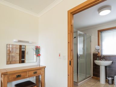 A wooden vanity table with a mirror and flowers next to a bathroom with shower and sink at Lovat Highland Bothy in Beauly