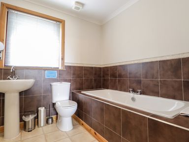 A bathroom with a white sink, toilet, and bathtub with brown tiles at Lovat Highland Bothy in Beauly