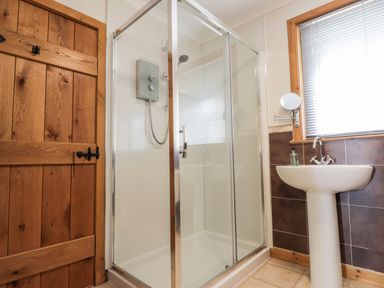 A bathroom with a glass shower enclosure a white pedestal sink a wooden door and a window with blinds at Lovat Highland Bothy in Beauly