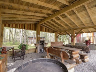 A wooden shelter with picnic tables wooden benches a brick barbecue and outdoor chairs at Lovat Highland Bothy in Beauly
