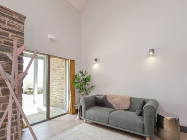 A living room with a gray sofa cushions and a throw blanket near sliding glass doors and a potted plant at Ben Luna Lodge in Drumnadrochit Loch Ness