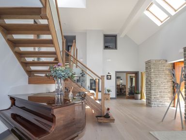 An interior room with a wooden staircase a grand piano with flowers on top stone wall and skylights at Ben Luna Lodge in Drumnadrochit Loch Ness