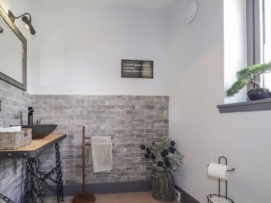 A bathroom with a wooden counter and black sink a towel holder with towel and a plant by the window at Ben Luna Lodge in Drumnadrochit Loch Ness