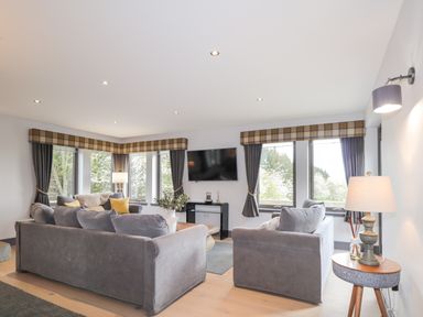 A living room with two gray sofas a round side table and a wall-mounted TV at Ben Luna Lodge in Drumnadrochit Loch Ness