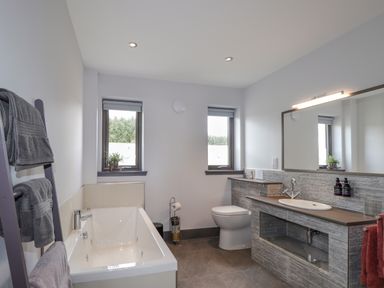 A bathroom with a bathtub, two windows, a toilet, a sink with a large mirror, and towels on a rack at Ben Luna Lodge in Drumnadrochit Loch Ness