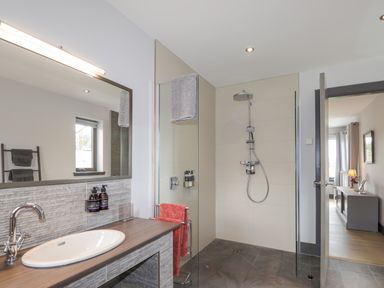 A bathroom with a sink, mirror, walk-in shower, towels, and a doorway leading to another room at Ben Luna Lodge in Drumnadrochit Loch Ness
