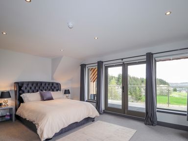 A bedroom with a large bed lamps on side tables and glass doors leading to a balcony at Ben Luna Lodge in Drumnadrochit Loch Ness