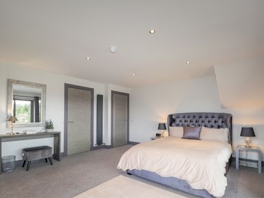 A bedroom with a bed nightstands with lamps a dressing table mirror stool and two doors at Ben Luna Lodge in Drumnadrochit Loch Ness