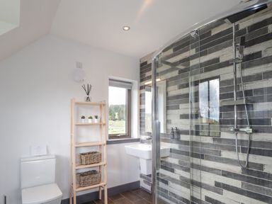 A bathroom with a toilet wooden shelving with plants and baskets a window a sink and a glass shower at Ben Luna Lodge in Drumnadrochit Loch Ness