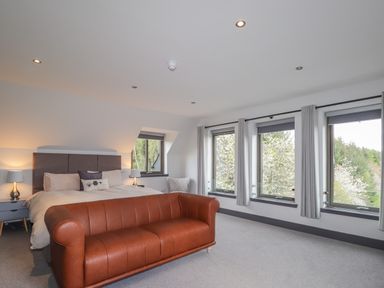 A bedroom with a bed bedside tables lamps a brown leather sofa and windows with curtains at Ben Luna Lodge in Drumnadrochit Loch Ness