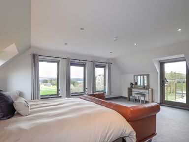 A bedroom with a large bed a brown leather bench windows with curtains a dressing table and a glass door leading outside at Ben Luna Lodge in Drumnadrochit Loch Ness
