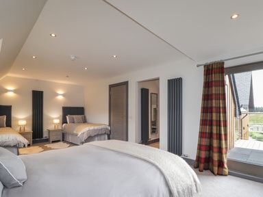 A bedroom with three beds bedside tables lamps a window with checkered curtains and wall radiators at Ben Luna Lodge in Drumnadrochit Loch Ness