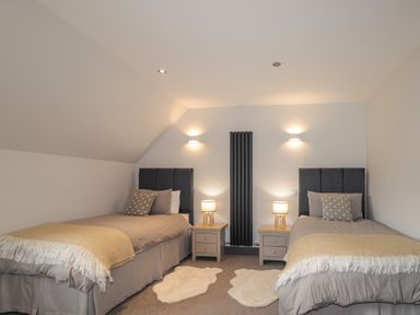 A bedroom with two single beds bedside tables lamps and a vertical radiator at Ben Luna Lodge in Drumnadrochit Loch Ness
