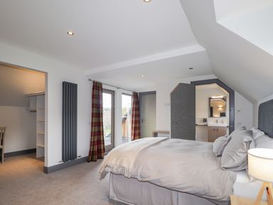 A bedroom with a bed a bedside lamp a walk-in closet and an en suite bathroom at Ben Luna Lodge in Drumnadrochit Loch Ness