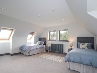 A bedroom with two single beds two nightstands with lamps a rug and windows at Ben Luna Lodge in Drumnadrochit Loch Ness