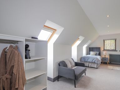 A bedroom with a single bed a gray loveseat an open wardrobe with brown robes and a hairdryer at Ben Luna Lodge in Drumnadrochit Loch Ness