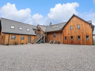 A wooden building with multiple windows and exterior stairs on a gravel ground at Ben Luna Lodge in Drumnadrochit Loch Ness