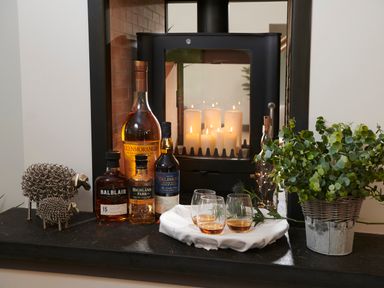 A hearth with bottles of whiskey glasses a metal sheep sculpture a plant and lit candles at Ben Luna Lodge in Drumnadrochit Loch Ness