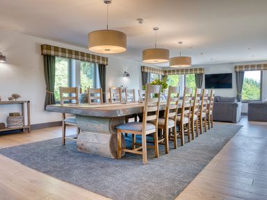 A dining room with a large wooden table and multiple wooden chairs with fabric cushions at Ben Luna Lodge in Drumnadrochit Loch Ness