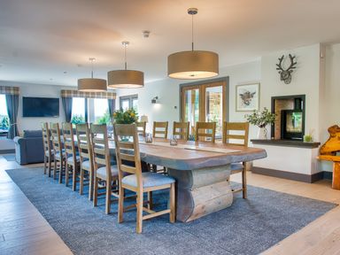 A dining room with a long wooden table and chairs under pendant lights at Ben Luna Lodge in Drumnadrochit Loch Ness
