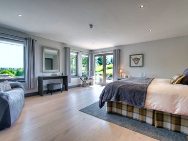 A bedroom with a bed a sofa a vanity table and large windows at Ben Luna Lodge in Drumnadrochit Loch Ness