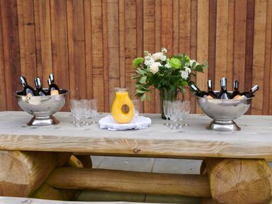 A wooden table with bottles in ice buckets glasses a pitcher of orange juice and a flower arrangement at Ben Luna Lodge in Drumnadrochit Loch Ness