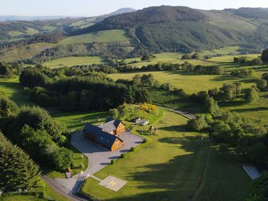 A large house surrounded by trees and grassy fields with hills in the background at Ben Luna Lodge in Drumnadrochit Loch Ness