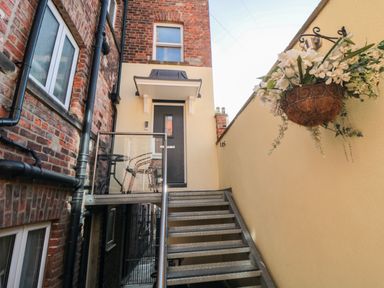 An outdoor staircase leading to a gray door with a small balcony and a hanging basket of flowers at Tower Apartment in Whitby