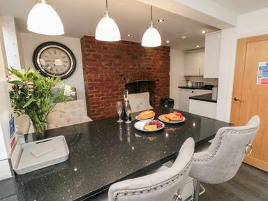 A kitchen with a black countertop island and gray chairs with a brick wall and a clock at Tower Apartment in Whitby