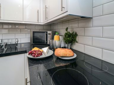 A kitchen counter with plates of bread cheese and grapes next to a microwave and a bottle of orange juice at Tower Apartment in Whitby