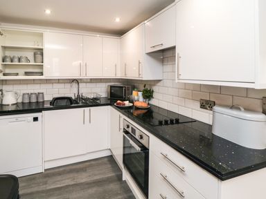 A kitchen with white cabinets black countertops and a tiled backsplash at Tower Apartment in Whitby