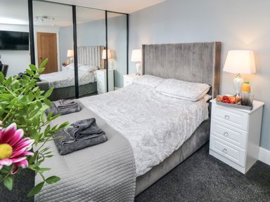A bedroom with a bed with gray headboard bedside tables lamps a mirror closet and a tray with food at Tower Apartment in Whitby