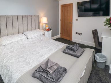 A bedroom with a bed folded towels on the foot of the bed a bedside table with a lamp and fruit a wall mounted television and a desk with a chair at Tower Apartment in Whitby