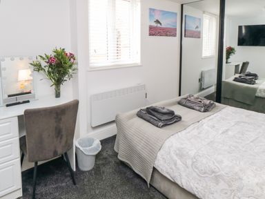 A bedroom with a bed, folded towels, a desk with a chair, flowers, and a wall mirror at Tower Apartment in Whitby