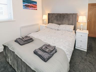 A bedroom with a double bed two bedside tables with lamps folded towels on the bed and a window at Tower Apartment in Whitby