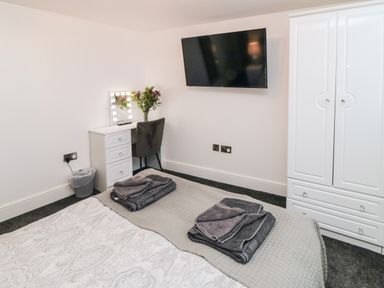 A bedroom with a bed towel stacks a white wardrobe a wall mounted television and a white desk with a chair at Tower Apartment in Whitby