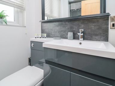 A bathroom sink with toiletries next to a toilet and a window with blinds at Tower Apartment in Whitby